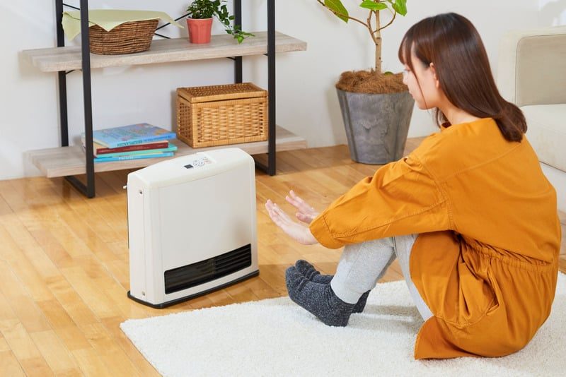 Homeowner adjusting a space heater in a warm living room